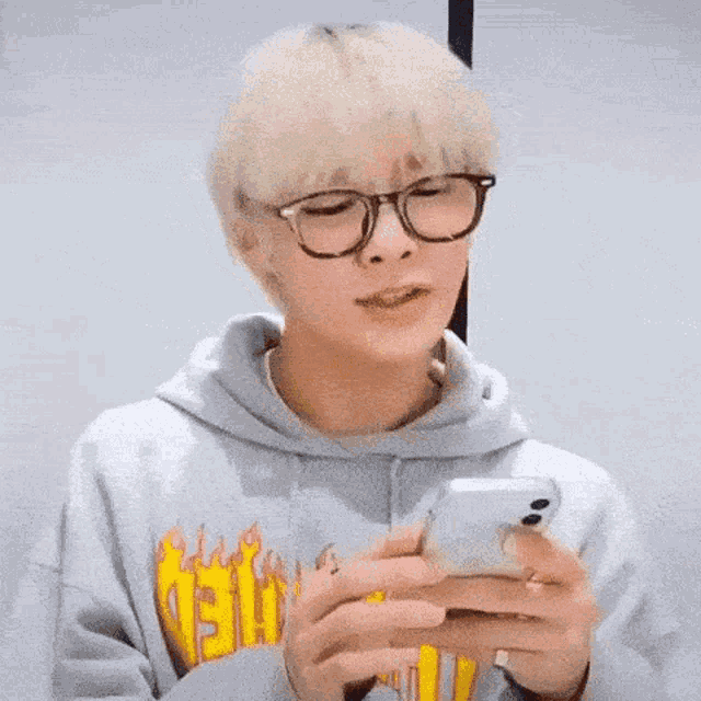 a young man wearing glasses and a hoodie is looking at his cell phone .