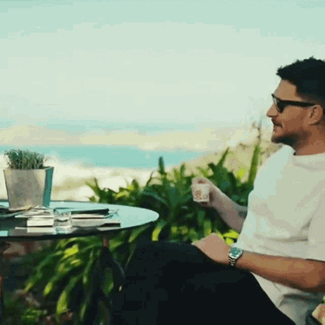 a man wearing sunglasses sits at a table holding a cup