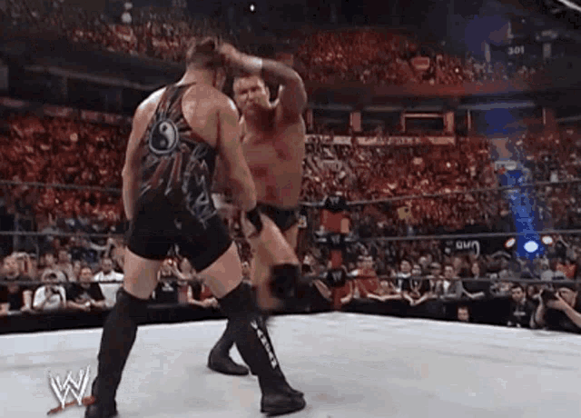 two wrestlers are fighting in a wrestling ring while a crowd watches .