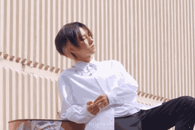 a man in a white shirt is sitting in front of a wall with the word hrlino on it