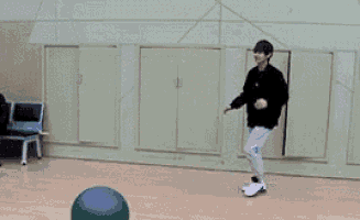 a man is kicking a ball in a gym while another man sits in a chair .