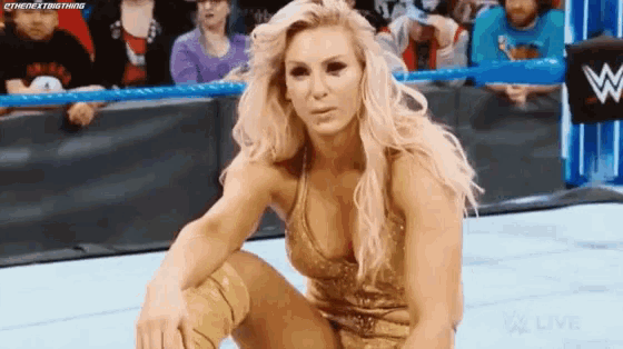 a woman in a gold dress is kneeling down in a wrestling ring in front of a crowd .