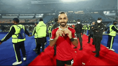 a man in a red shirt with the number 10 on his shorts stands on a red carpet