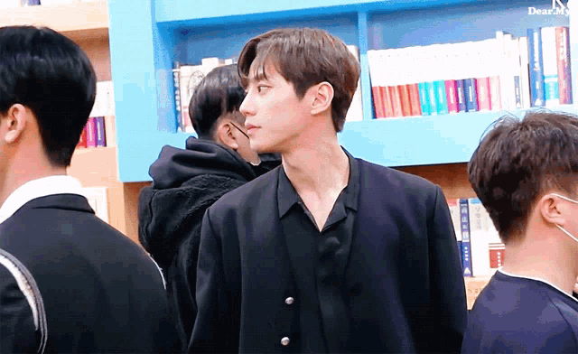 a man in a black jacket stands in front of a bookshelf with the word dear on the bottom