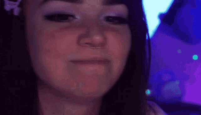 a close up of a woman 's face with her hands on her ears and a purple background .