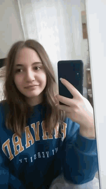 a girl is taking a selfie in front of a mirror wearing a blue sweatshirt with the word ravens on it
