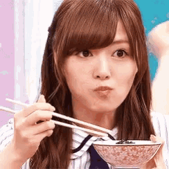 a woman is holding a bowl of food with chopsticks .