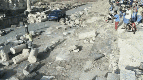 a group of people standing around a rocky area with a jeep parked in the background