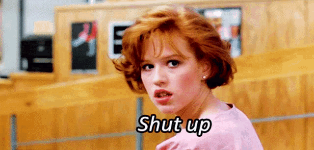 a woman with red hair is standing in front of a wooden wall and saying shut up .