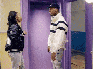 a man and a woman are standing in front of a purple door and talking to each other .