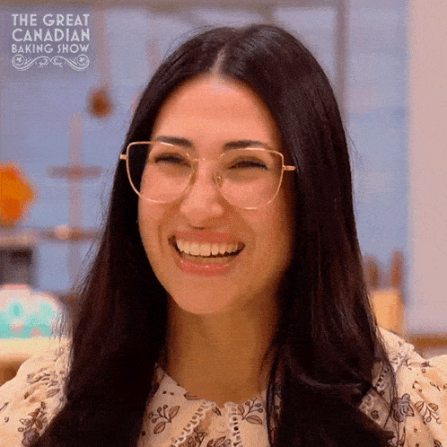 a woman wearing glasses is smiling in front of the great canadian baking show logo .