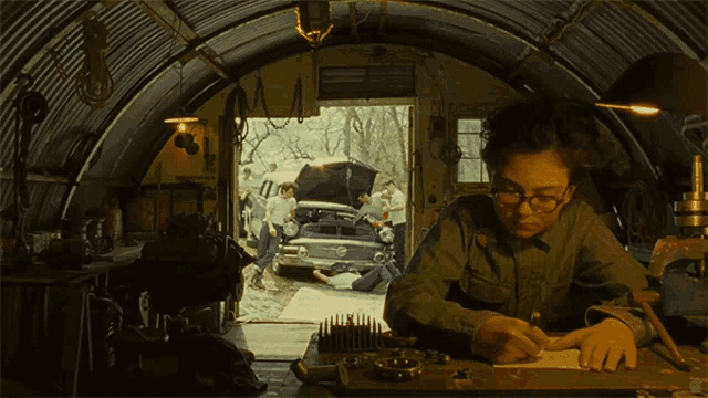 a man wearing glasses sits at a desk in a garage