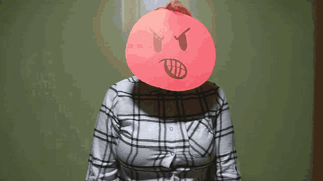 a woman wearing a plaid shirt has an angry face drawn on a piece of paper