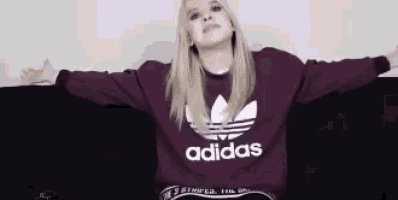 a woman is sitting on a couch with her arms outstretched wearing an adidas sweater .