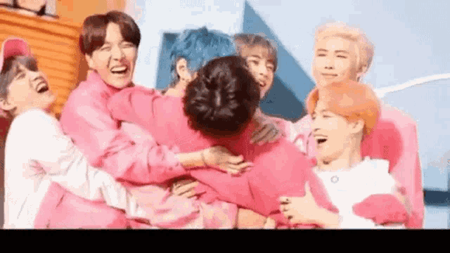a group of young men are hugging each other while wearing pink shirts .