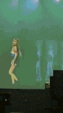a woman dancing on a stage with a green background
