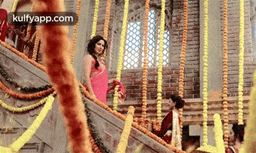 a woman in a red saree is walking down a set of stairs decorated with flowers .