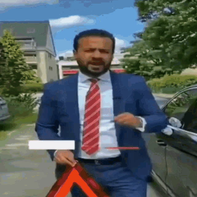 a man in a suit and tie is standing next to a car holding a red triangle