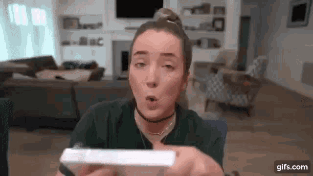 a woman in a green shirt is holding a white box in her hands in a living room .