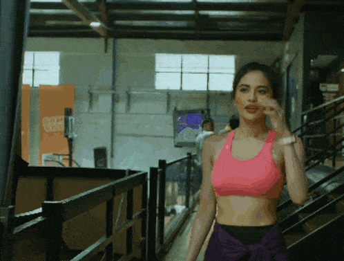 a woman in a pink sports bra walks down stairs in a gym