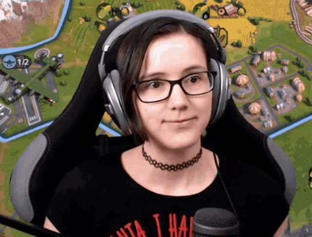 a woman wearing headphones and a choker is sitting in front of a screen that says 1/2