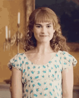 a woman in a blue and white floral dress is smiling and looking at the camera .