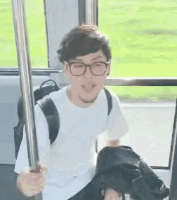a man wearing glasses and a backpack is sitting on a bus holding a railing .