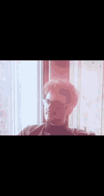 a man wearing glasses and a turtleneck is smiling in front of a window
