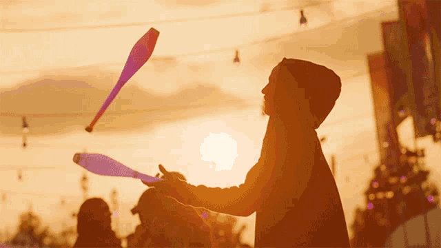 a man in a hoodie is juggling two clubs at a carnival