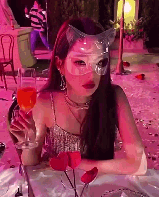 the woman is wearing a cat mask and holding a glass of wine .