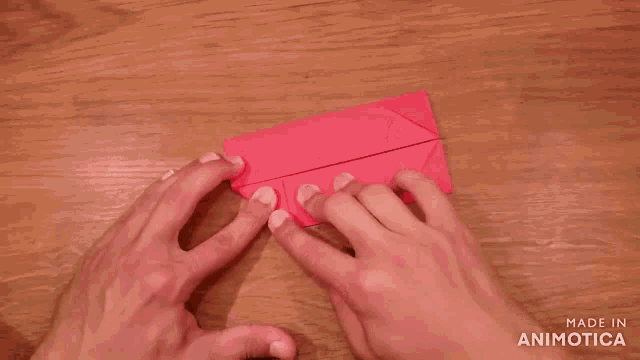 a person is folding a piece of red paper on a wooden table and the words made in animatica are visible