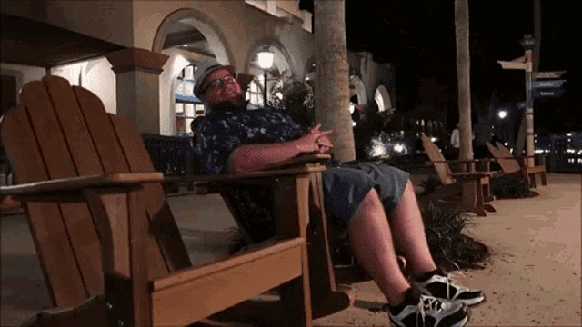 a man sits in an adirondack chair in front of a building with a sign that says ' sunset '