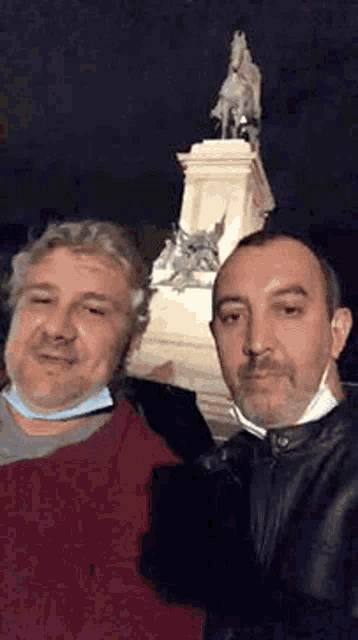 two men are posing for a selfie in front of a statue .