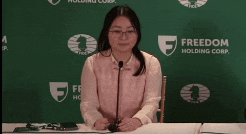 a woman sitting at a table with a microphone in front of a freedom holding corp. sign