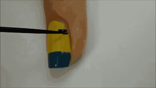 a yellow and blue nail being painted with a black brush