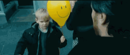a child is holding a yellow balloon with a smiley face on it .