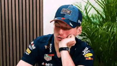a man wearing a baseball cap and a blue shirt is sitting with his hand on his chin .