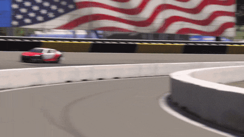 a race car is going around a curve on a track with an american flag behind it