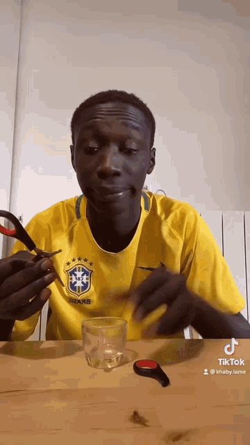 a man in a yellow shirt is holding a pair of scissors over a glass .