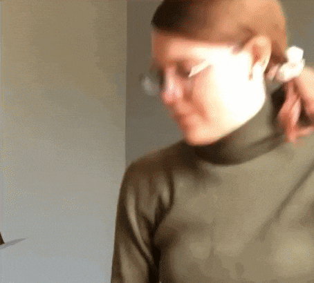 a woman wearing a turtleneck and glasses is holding her hair .