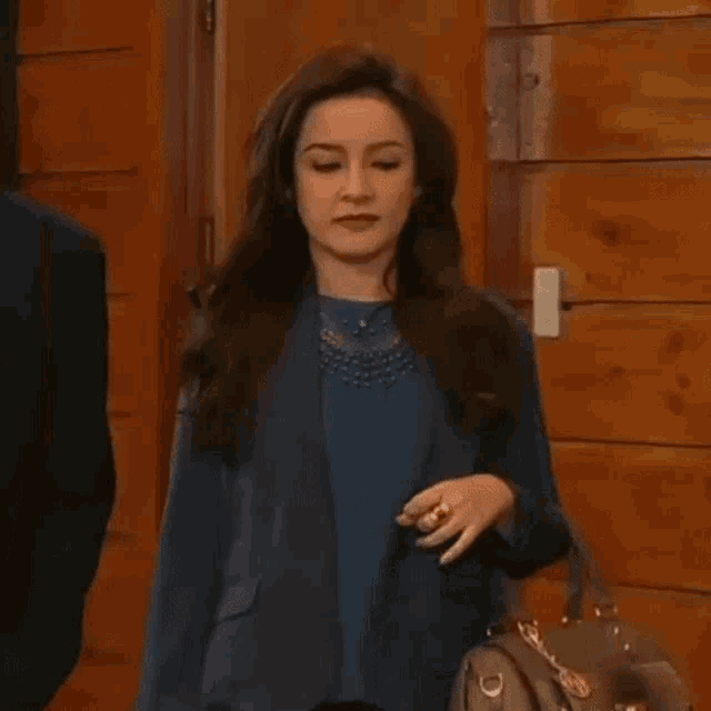 a woman in a blue jacket is holding a purse and a ring .