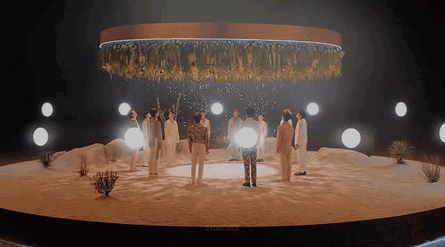 a group of people standing in a circle with flowers hanging from the ceiling behind them