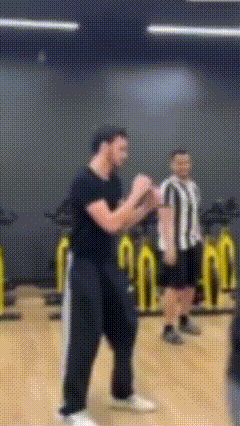 a man in a black shirt is standing in a gym with a referee behind him .
