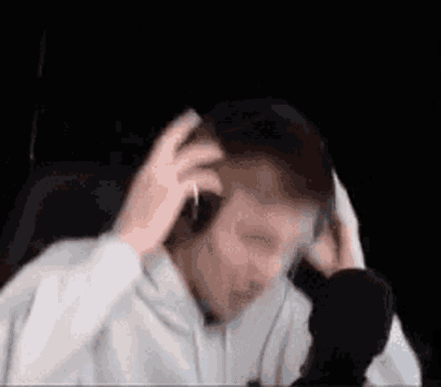 a man wearing headphones is sitting in front of a microphone and scratching his head .
