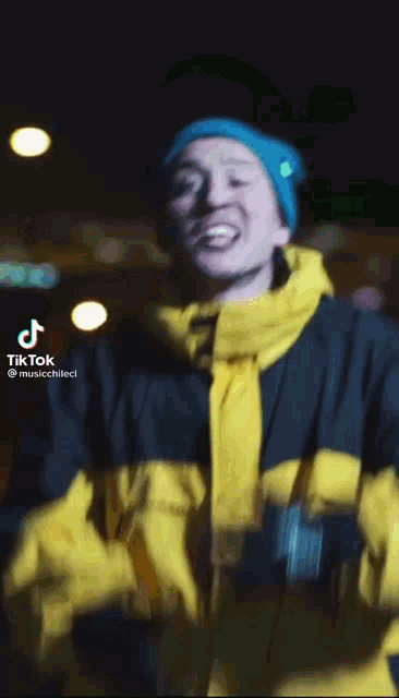 a man wearing a blue beanie and a yellow jacket has tiktok written on the bottom
