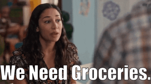 a woman is sitting at a table talking to a man and the words we need groceries are on the screen .