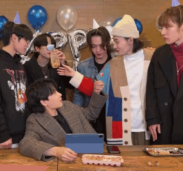 a group of young men are gathered around a table with balloons and a sign that says happy birthday