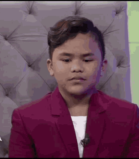 a young boy in a purple suit is sitting in a chair making a funny face .