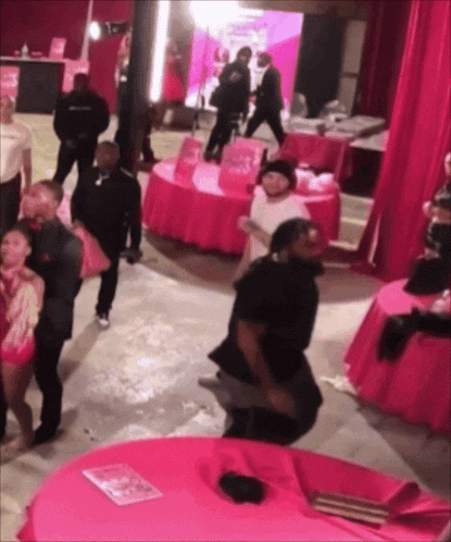 a group of people are gathered in a room with pink tables and curtains