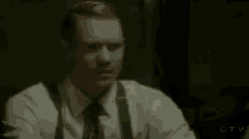 a man in a white shirt and black tie is sitting at a table with his arms outstretched .